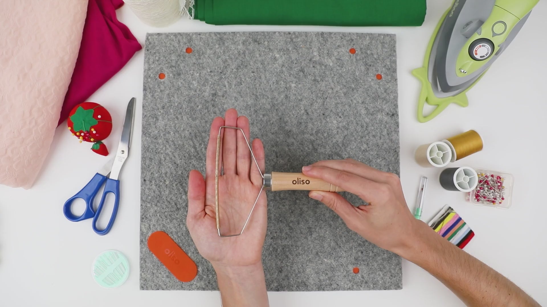Video demonstration of the Oliso MultiMat cleaning tool effortlessly removing lint, threads, and pet hair from a wool pressing mat using its dual metal comb head and ergonomic wood handle.